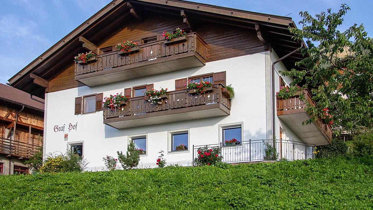 La nostra casa in mezzo ai prati verdi in piena estate. Le rose sono in fiore e i gerani fioriscono sul balcone. 