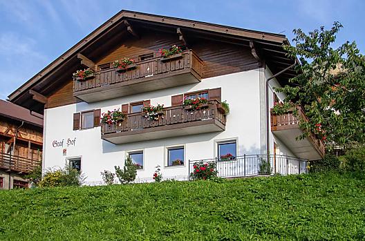 La nostra casa in mezzo ai prati verdi in piena estate. Le rose sono in fiore e i gerani fioriscono sul balcone. 