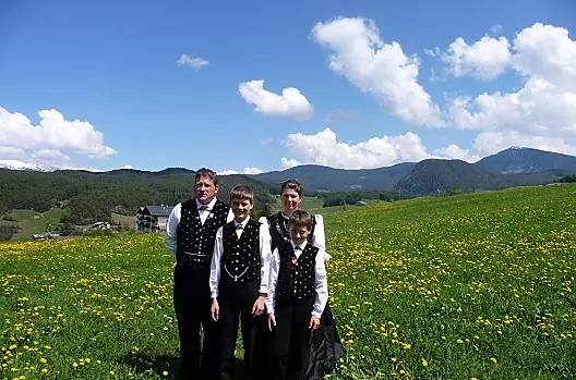 Prato verde con denti di leone in fiore al Wegmacherhof. La famiglia Gabloner in costume tradizionale in occasione della Santa Cresima di Florian.