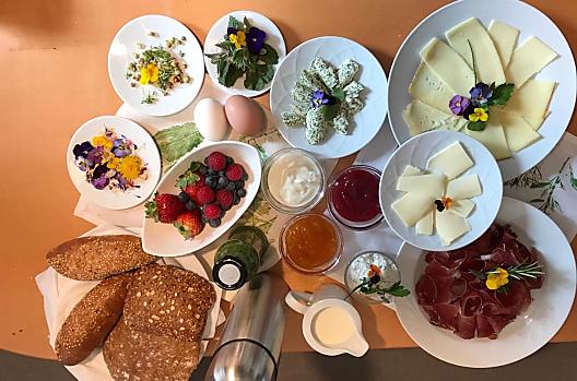 Cestino della colazione con frutti di bosco biologici freschi, burro alle erbe, quark alle erbe, smoothie alle erbe, fiori commestibili ed erbe fresche.