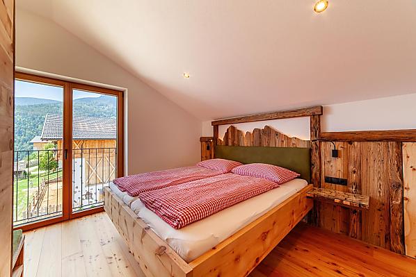 Doppelbett mit französischem Balkon und Blick zu Stall und Bergen.
