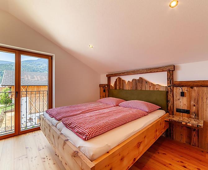 Doppelbett mit französischem Balkon und Blick zu Stall und Bergen.