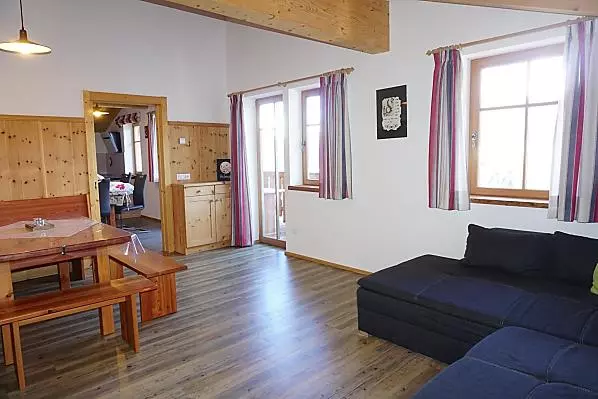 Wohnzimmer mit Panoramablick, großem Sofa, Tisch und Sitzecke in Lärchen- und Zirbenholz sowie TV. 