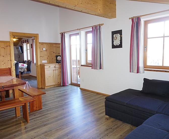 Wohnzimmer mit Panoramablick, großem Sofa, Tisch und Sitzecke in Lärchen- und Zirbenholz sowie TV. 