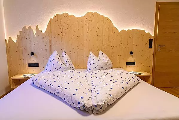 Kuschliges Doppelbettzimmer mit Bergumriss aus Holz und Beleuchtung.