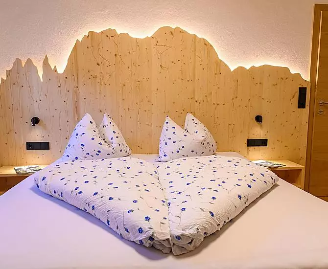 Kuschliges Doppelbettzimmer mit Bergumriss aus Holz und Beleuchtung.