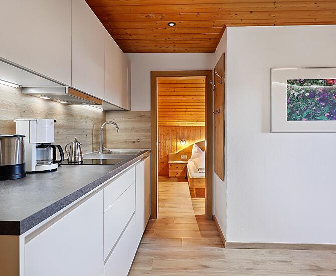 Küchenzeile mit Wasserkocher, Kaffeemaschine, Spülmaschine, Kühlschrank mit Gefrierfach, und Herdpatte.